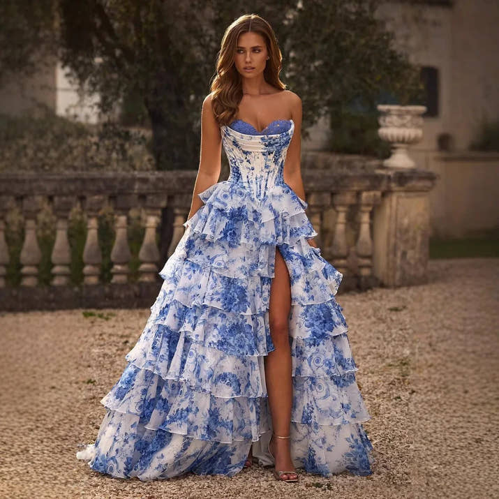 Woman wearing a blue floral gown with a high slit in an outdoor setting.